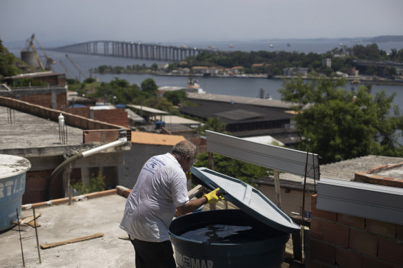 Augusto Cesar, a city worker who combats endemic diseases, inspects a water tank where mosquitoes can breed in the Morro da Penha favela in Niteroi, Brazil, the Rio-Niteroi Bridge in the background.