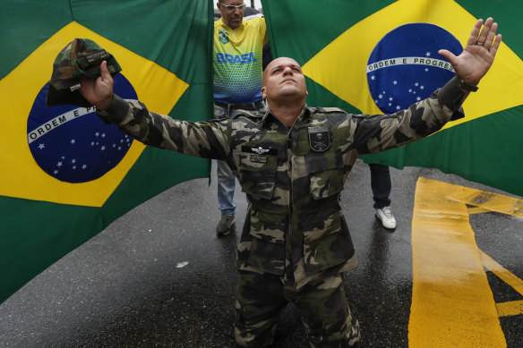 A Bolsonaro supporter dressed in fatigues, kneels in front of national flags in Rio de Janeiro, during a protest against his defeat in the presidential election.