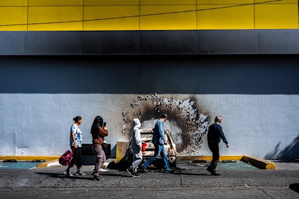 People walk past a burnt-out car at a shopping centre in Guadalajara.