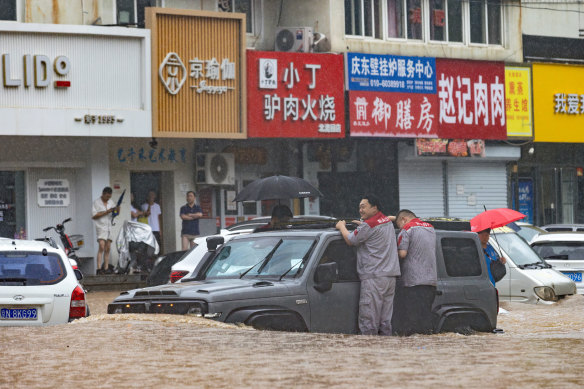 Men hang on as they travel through a flooded street in a Beijing suburb where days of heavy rain from remnants of typhoon Doksuri have caused heavy damage.