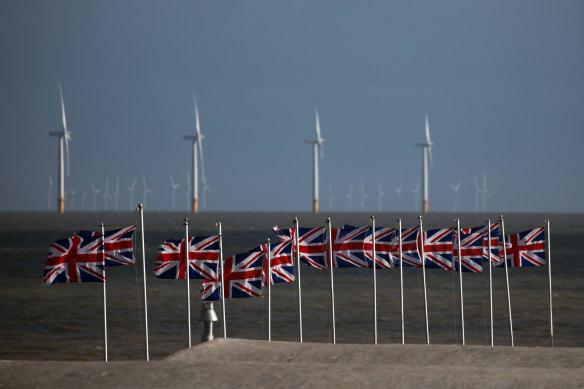 British Unio<em></em>n flags, also known as Unio<em></em>n Jacks, fly against a backdrop of offshore wind turbines off the coast in Clacton On Sea, England.