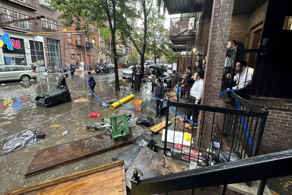 Residents watch as workers attempt to clear a drain in flood waters in Brooklyn.
