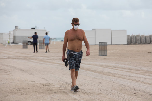 A man wears a protective mask while walking along the beach in Miami Beach, Florida.