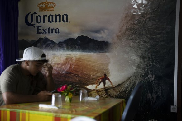 A customer sits at the only snack bar in Teahupo’o, Tahiti. The village is expecting an influx of tourists for the Olympic Games.