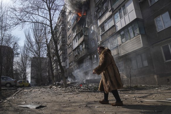 A woman walks past a burning apartment building after shelling in Mariupol.
