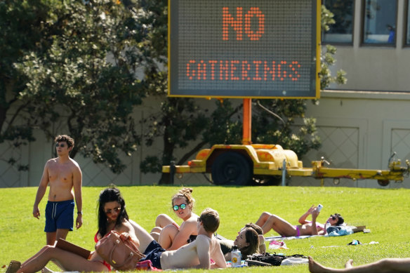 Groups of people sunbathe at St Kilda in Melbourne on Saturday in front of a sign warning against gathering on the foreshore.