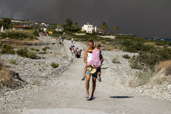 A man carries a child as they leave an area where a forest fire burns, on the island of Rhodes, Greece.