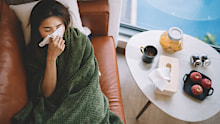 an sick asian chinese female lying on sofa in living room covered with blanket and wiping nose with tissue paper