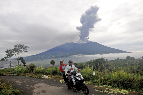 Motorists ride past by as Mount Marapi spews volcanic materials.