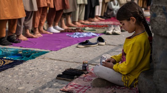 An Afghan girl working as a shoe cleaner sits in the street while men pray during Friday prayers in Kabul, Afghanistan, last week.