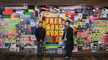 Two pro-democracy protesters stand in front of a "Lennon Wall" at the University of Technology Sydney.