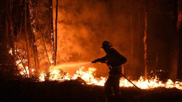 A NSW RFS fire fighter work through Thursday night to prevent a flare crossing the Kings Highway in between Nelligen and Batemans Bay. Australia's largest insurer says it has already received $400 million in claims.