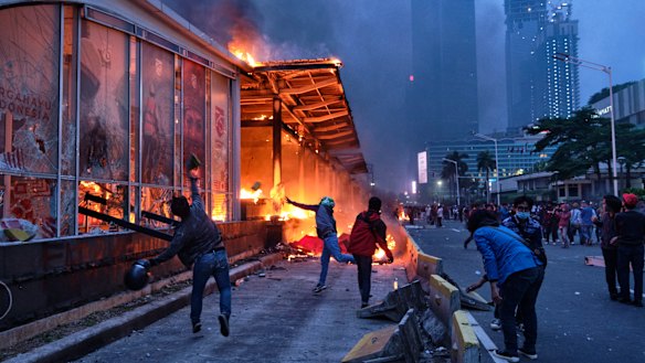 Rioters throw rocks at a burning bus station near the Welcome Monument in central Jakarta. Protesters have gathered across Indonesia after the government passed labor laws it claims will boost economic recovery needed due to coronavirus. 