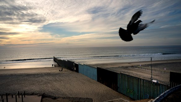 A pigeon flies near the border wall that separates Mexico, left, from the US, where the wall ends in the Pacific Ocean, seen from Tijuana, Mexico.