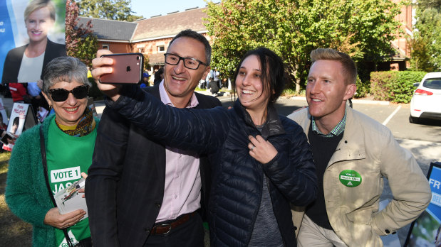 Greens leader Richard Di Natale (centre) smiles for a selfie with their hope for Higgins, Jason Ball (right).