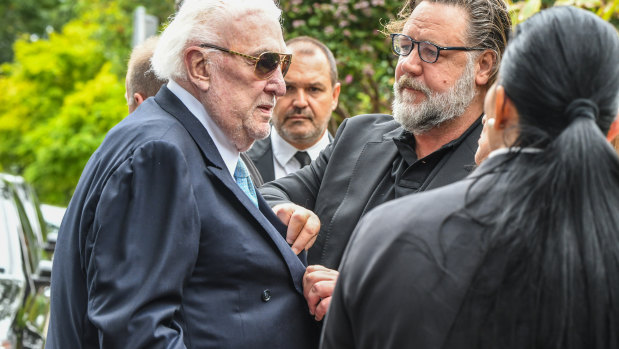 Russell Crowe leans over to hug and do up some buttons on broadcaster John Laws' jacket at the funeral of Caroline Laws on Tuesday. 