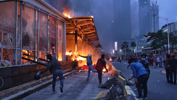 Rioters throw rocks at a burning bus station near the Welcome Monument in central Jakarta. Protesters have gathered across Indonesia after the government passed labor laws it claims will boost economic recovery needed due to coronavirus. 