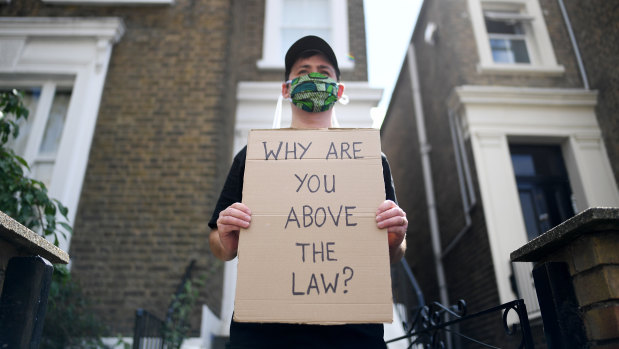 A protester holds up a placard which reads 'Why are you above the law?' outside the home of Dominic Cummings.