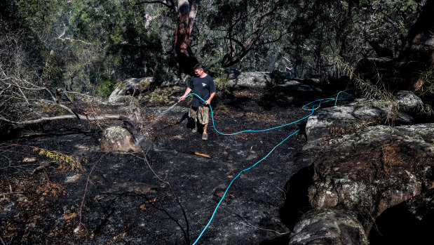 Justin Frith hoses down an area behind his home in Menai in Sydney.