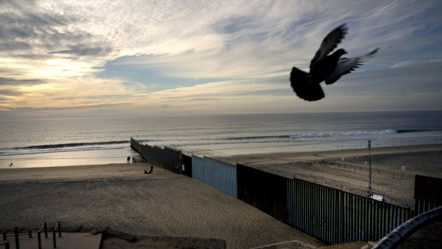 A pigeon flies near the border wall that separates Mexico, left, from the US, where the wall ends in the Pacific Ocean, seen from Tijuana, Mexico.