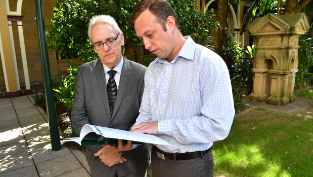 Former District Court judge Michael Forde (left) hands a report into Queensland's towing industry to then-acting minister for Main Roads Steven Miles (right) in August 2017.