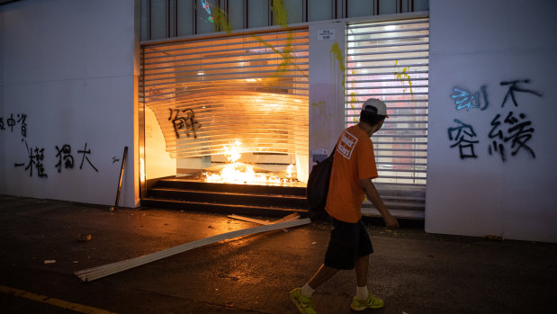 A man walks in front of a branch of Bank of China set ablaze during a protest against a government ban on face masks. 
