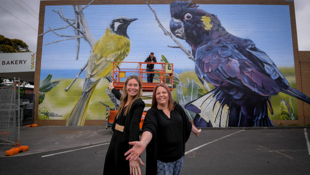 Wonthaggi Business and Tourism Association president Amy Easton (left) and bakery co-owner Dee Connell in front of Jimmy Dvate and his artwork in Wonthaggi. 