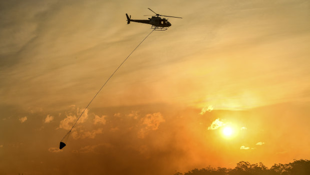 A helicopter water bombs a bushfire threatening homes in Sydney's south-west in April 2018.