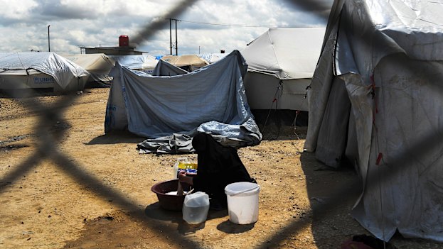 A woman washes clothes in front of her tent at the fence line of the Foreign section of al-Hawl camp in Syria.