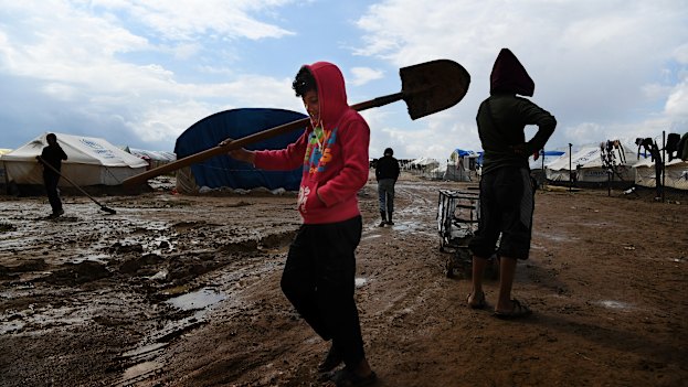 Children carry tools through the mud at the squalid al-Hawl camp.