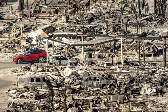 A car drives past homes and vehicles destroyed by the Palisades Fire.