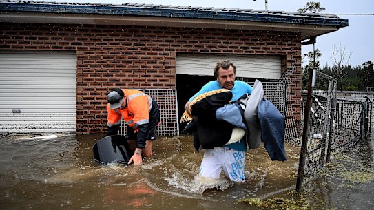 James Larking (right), with the help of Dylan Smith. evacuates his flooded home in Pampoolah.