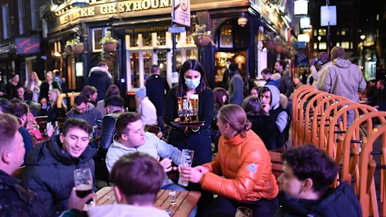 A waitress serves drinks as customers sit at setup tables outside pubs in Soho, in London, on the day some of England’s third coronavirus lockdown restrictions were eased.