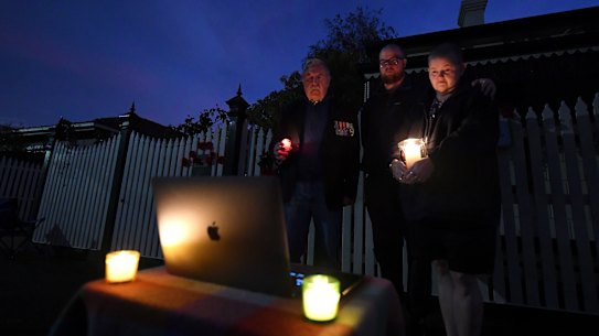 Vietnam veteran Rod Coote, son Nathan and wife Julie observe a live stream of ANZAC day's dawn service outside their house in Melbourne on Saturday.