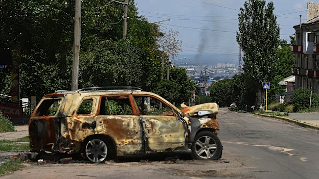 The remains of a vehicle on a road in Lysychansk where smoke can be seen rising from the besieged city of Sievierodonetsk.