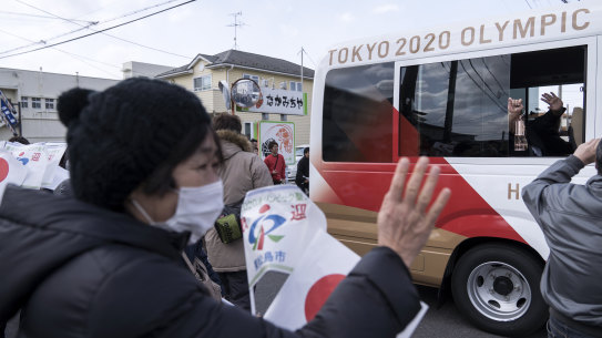 A woman waves to a bus transporting Japanese comedy duo Sandwich Man holding the Olympic flame after the Tokyo 2020 Olympic Games torch arrival ceremony in Matsushima on March 20.