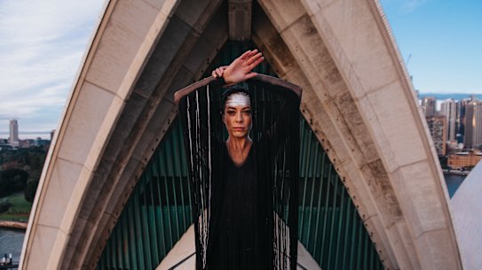 Pictured is Bangarra dancer Courtney Radford on top of one of the Opera House sails in full costume, early this morning.