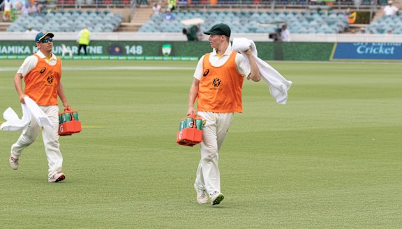 Substitute fielders Dan Leerdam and Tom Vane-Tempest run drinks out to the Australian cricket team after the dismissal of Dhananjaya de Silva on day four of the test between Australia and Sri Lanka. 