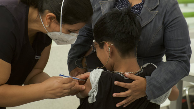 A healthcare worker injects a boy with a dose of the Pfizer COVID-19 vaccine in Mexico.