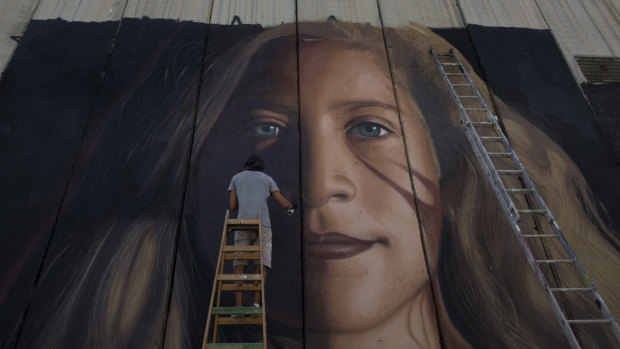 An artist paints a giant mural of prominent Palestinian activist Ahed Tamimi on part of the Israeli separation wall, in the West Bank city of Bethlehem on  July 25.