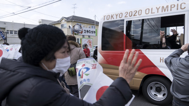 A woman waves to a bus transporting Japanese comedy duo Sandwich Man holding the Olympic flame after the Tokyo 2020 Olympic Games torch arrival ceremony in Matsushima on March 20.