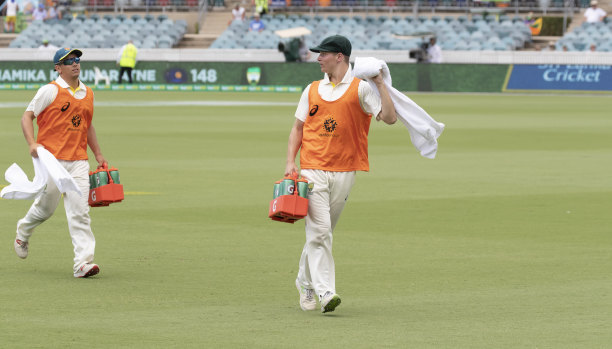 Substitute fielders Dan Leerdam and Tom Vane-Tempest run drinks out to the Australian cricket team after the dismissal of Dhananjaya de Silva on day four of the test between Australia and Sri Lanka. 