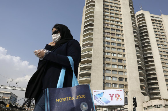 A pedestrian wearing a face mask crosses a street in northern Tehran.