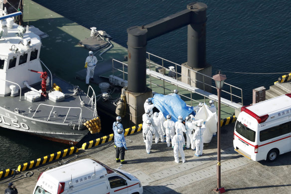 Medical workers in protective suits lead a passenger tested positive for a new coronavirus from the cruise ship Diamond Princess at Yokohama.