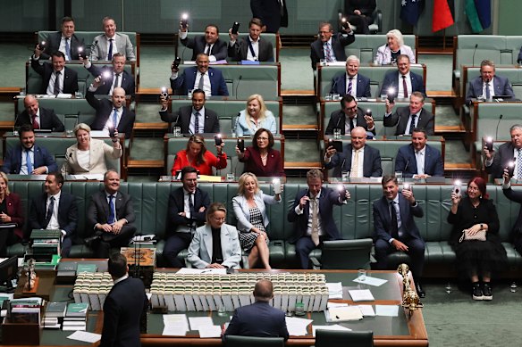 Members on the opposition benches turn on the lights on their phones after some of the lights in the chamber went off.