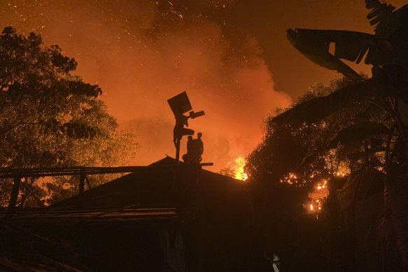 A Rohingya refugee hangs on to a pole trying to dismantle a solar panel and lamp as a fire blazes through their refugee camp at Kutupalong in Cox’s Bazar district, Bangladesh on Sunday.
