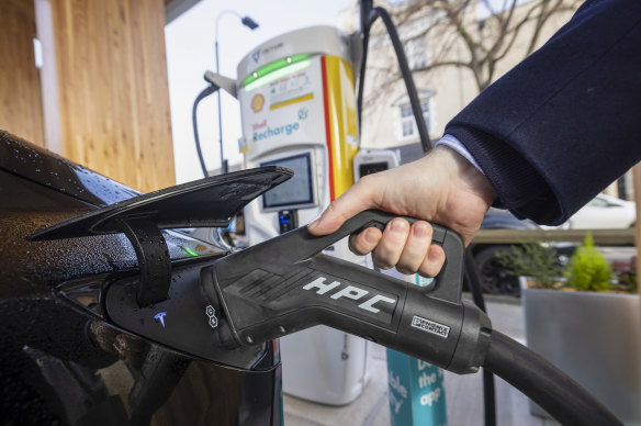 A customer places a charger into a vehicle at a Shell Recharge electric vehicle charging hub in London.