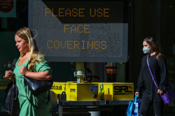 A woman wearing a protective face mask passes a sign reading "Please Use Face Coverings" in the financial district in the City of London.