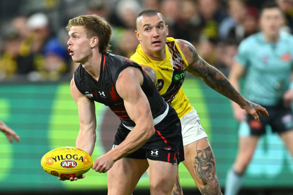 Ben Hobbs of the Bombers handballs whilst being tackled by Dustin Martin.