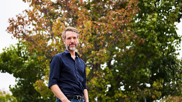 ANU lecturer of environmental measurement Matthew Brookhouse stands beside a flowering pear tree which is starting to change for autumn. 